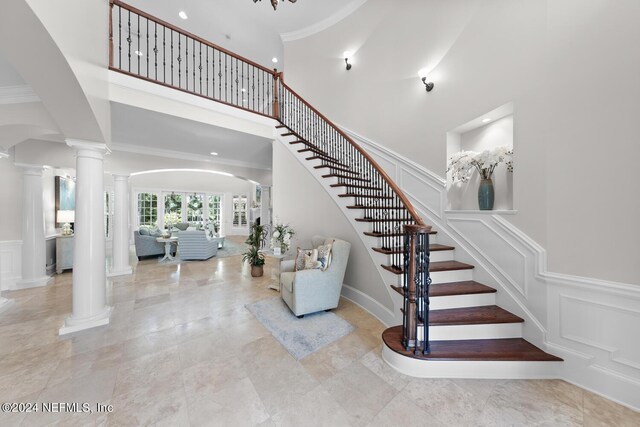 stairway with a towering ceiling, decorative columns, and ornamental molding