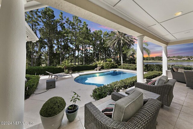 pool at dusk with an outdoor hangout area, a patio, and a water view