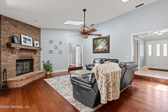 living room featuring dark hardwood / wood-style flooring, a brick fireplace, lofted ceiling with skylight, and ceiling fan