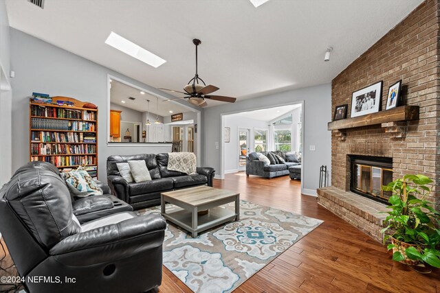 living room featuring hardwood / wood-style floors, vaulted ceiling with skylight, a fireplace, and brick wall