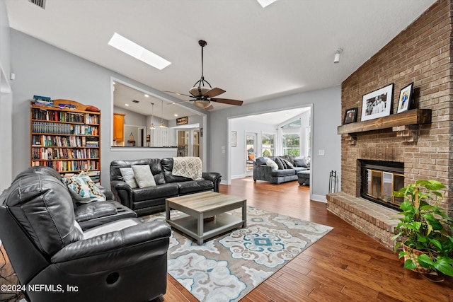 living room featuring lofted ceiling with skylight, a ceiling fan, a brick fireplace, wood finished floors, and baseboards