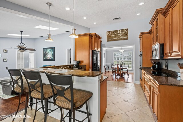 kitchen featuring dark stone countertops, light hardwood / wood-style flooring, decorative light fixtures, black appliances, and kitchen peninsula