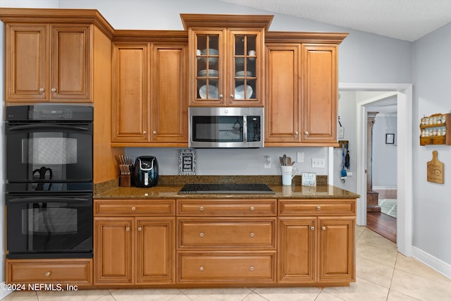 kitchen with black appliances, lofted ceiling, light tile patterned floors, and dark stone counters