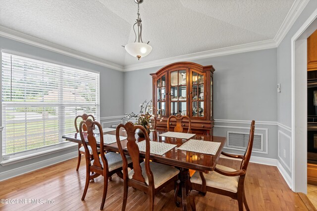 dining area featuring a textured ceiling, ornamental molding, and light hardwood / wood-style floors