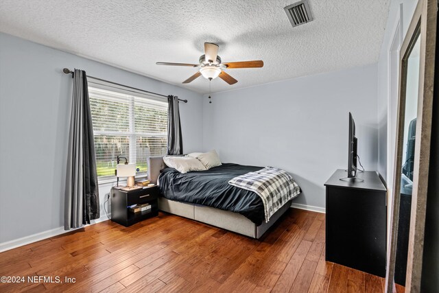 bedroom with a textured ceiling, dark wood-type flooring, and ceiling fan