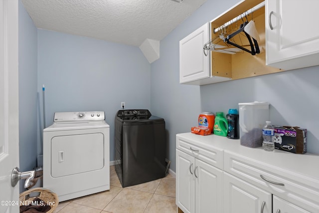 clothes washing area featuring a textured ceiling, cabinets, washer and clothes dryer, and light tile patterned flooring