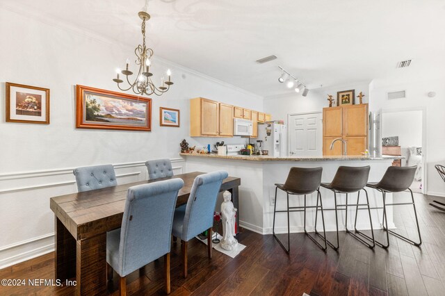 dining space featuring crown molding, dark wood-type flooring, rail lighting, and a notable chandelier