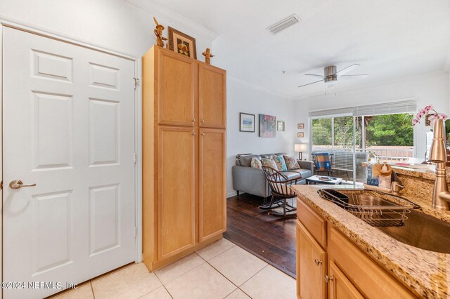 kitchen featuring light wood-type flooring, ornamental molding, light stone counters, sink, and ceiling fan