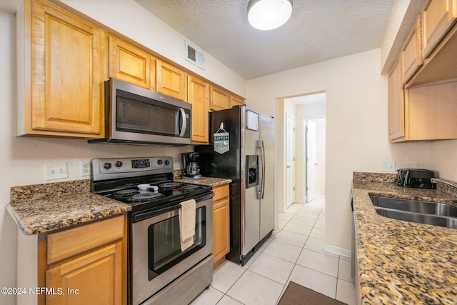 kitchen featuring dark stone countertops, a textured ceiling, light tile patterned floors, stainless steel appliances, and sink