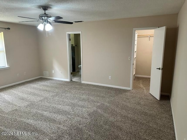 unfurnished bedroom featuring a textured ceiling, ensuite bath, ceiling fan, carpet flooring, and a spacious closet