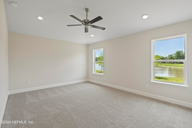 spare room with a water view, ceiling fan, and light colored carpet