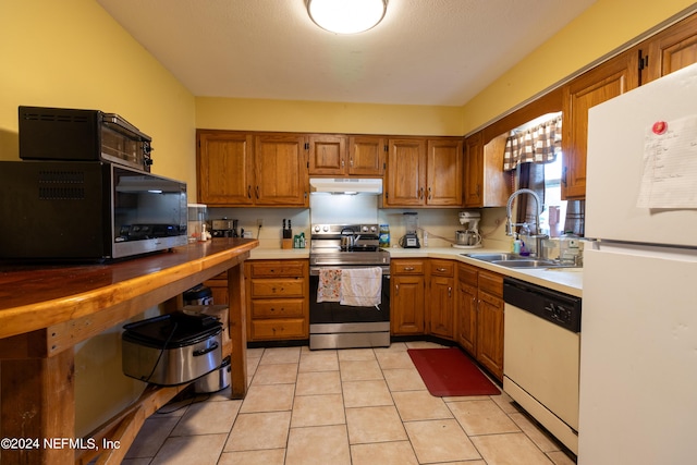 kitchen featuring white appliances, brown cabinets, under cabinet range hood, and a sink