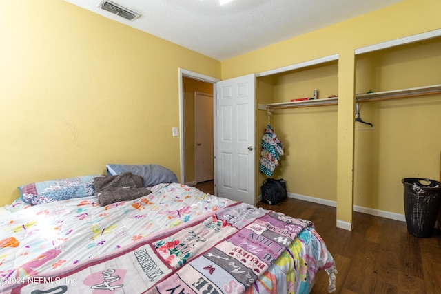 bedroom with visible vents, baseboards, multiple closets, and wood finished floors