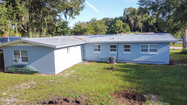 back of property with concrete block siding, cooling unit, central air condition unit, a lawn, and metal roof