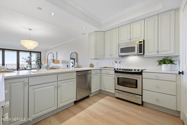 kitchen with light wood-type flooring, ornamental molding, decorative light fixtures, an inviting chandelier, and appliances with stainless steel finishes