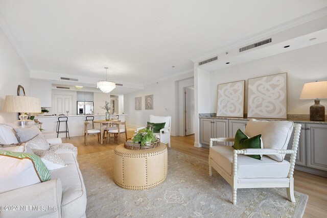 living room with light wood-type flooring, ornamental molding, and an inviting chandelier