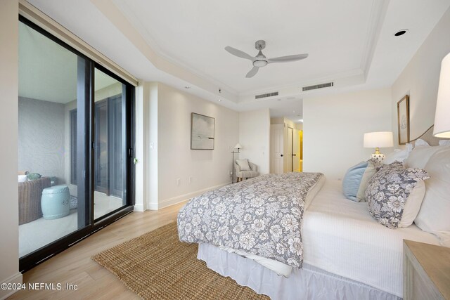 bedroom featuring multiple windows, light wood-type flooring, a raised ceiling, access to exterior, and ceiling fan