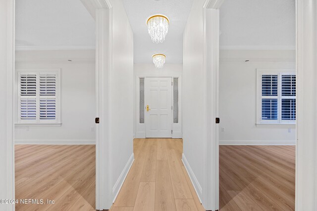 hall featuring ornamental molding, light hardwood / wood-style flooring, and an inviting chandelier