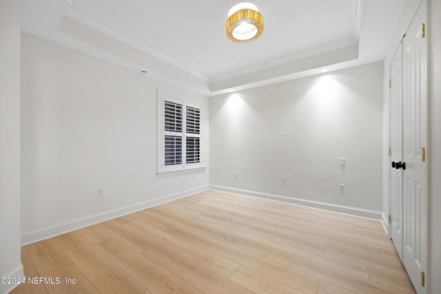 empty room featuring a raised ceiling, crown molding, and light hardwood / wood-style flooring