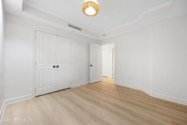 unfurnished bedroom with a closet, ornamental molding, a raised ceiling, and light hardwood / wood-style flooring