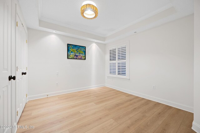 spare room featuring ornamental molding, a raised ceiling, and light hardwood / wood-style flooring