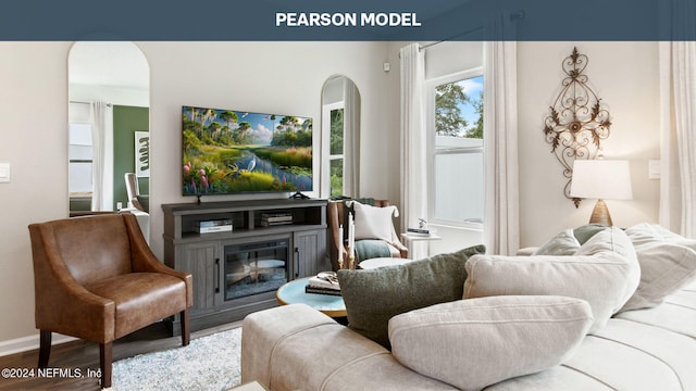 living area with arched walkways, a glass covered fireplace, wood finished floors, and baseboards