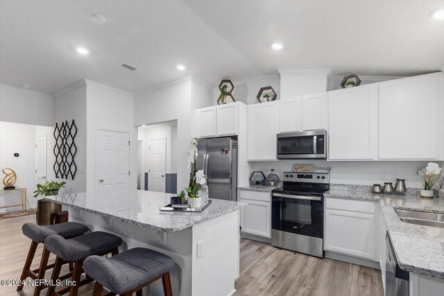 kitchen with appliances with stainless steel finishes, lofted ceiling, light hardwood / wood-style flooring, and a kitchen island