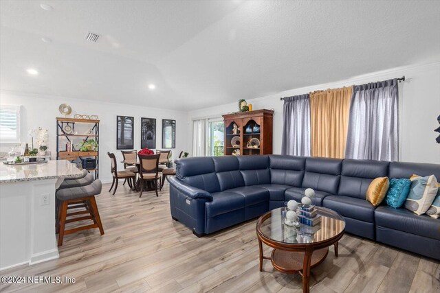 living room with lofted ceiling, ornamental molding, and light wood-type flooring