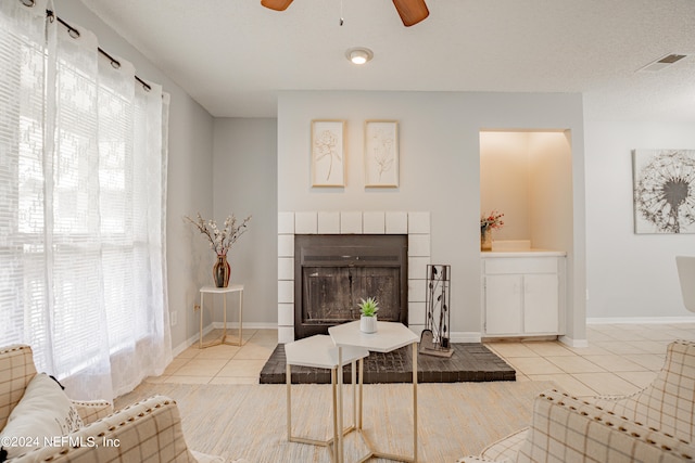 tiled living room featuring a textured ceiling, ceiling fan, and a tile fireplace