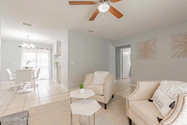 tiled living room with ceiling fan with notable chandelier and a textured ceiling