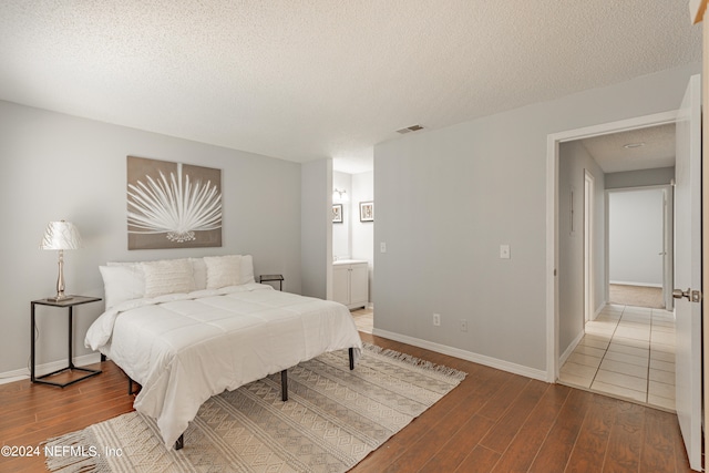 bedroom featuring hardwood / wood-style floors, ensuite bathroom, and a textured ceiling