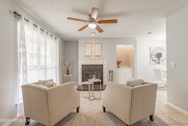 living room with a fireplace, a textured ceiling, light tile patterned flooring, and ceiling fan