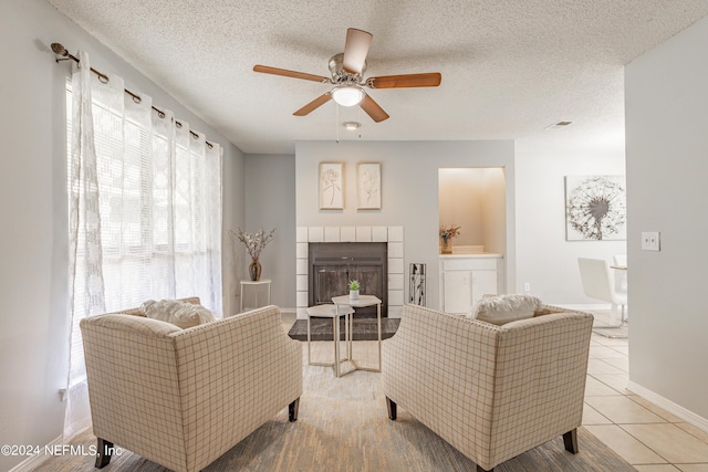 living area with a fireplace, a ceiling fan, a textured ceiling, tile patterned flooring, and baseboards