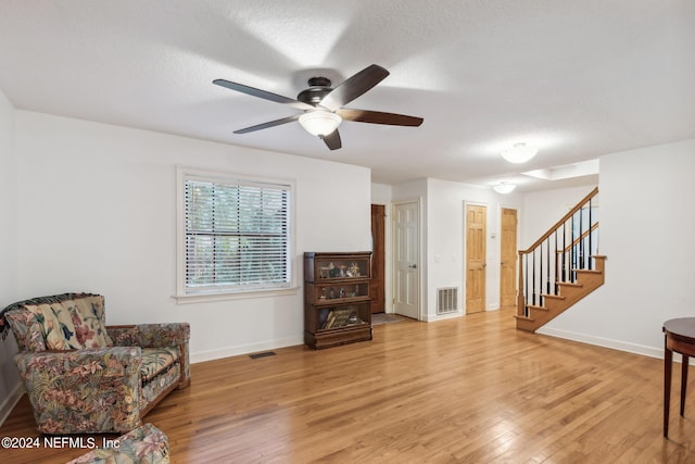 living area with light wood-type flooring, ceiling fan, and a textured ceiling