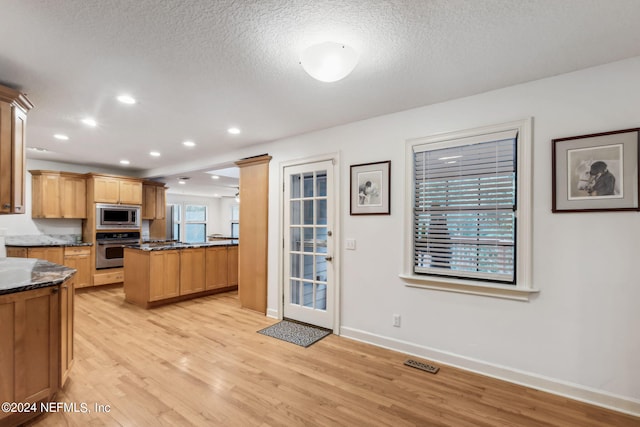 kitchen featuring dark stone countertops, a textured ceiling, stainless steel appliances, and light hardwood / wood-style flooring