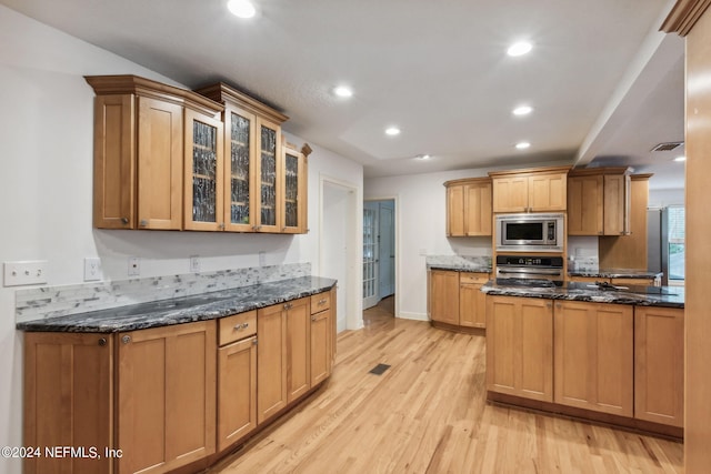 kitchen with stainless steel appliances, dark stone countertops, and light wood-type flooring