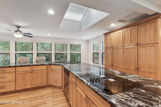 kitchen featuring black electric cooktop, dark stone countertops, light wood-type flooring, ceiling fan, and a skylight