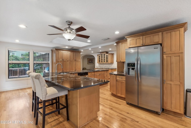 kitchen with ceiling fan, sink, stainless steel refrigerator with ice dispenser, a breakfast bar area, and light hardwood / wood-style floors