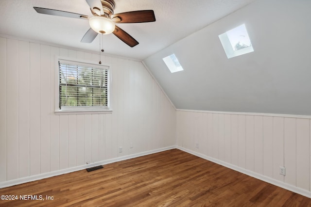 additional living space with ceiling fan, lofted ceiling with skylight, wood walls, and hardwood / wood-style floors