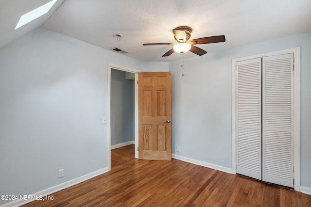 unfurnished bedroom with lofted ceiling with skylight, ceiling fan, a closet, and hardwood / wood-style flooring