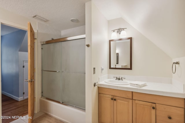 bathroom with vaulted ceiling, vanity, a textured ceiling, combined bath / shower with glass door, and hardwood / wood-style floors