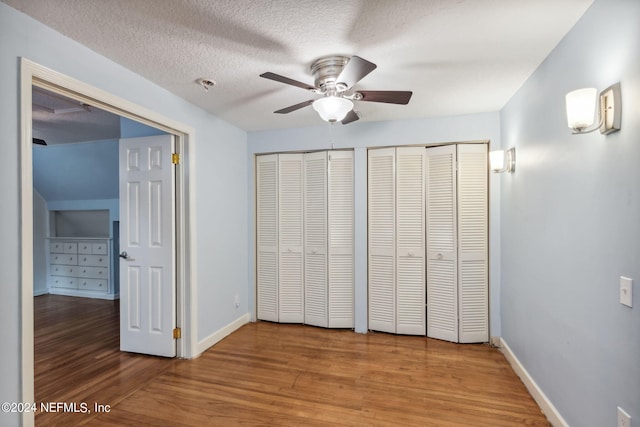 unfurnished bedroom featuring ceiling fan, multiple closets, hardwood / wood-style flooring, and a textured ceiling