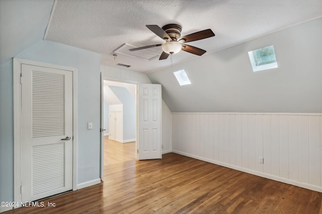 bonus room featuring a textured ceiling, hardwood / wood-style flooring, wood walls, lofted ceiling with skylight, and ceiling fan