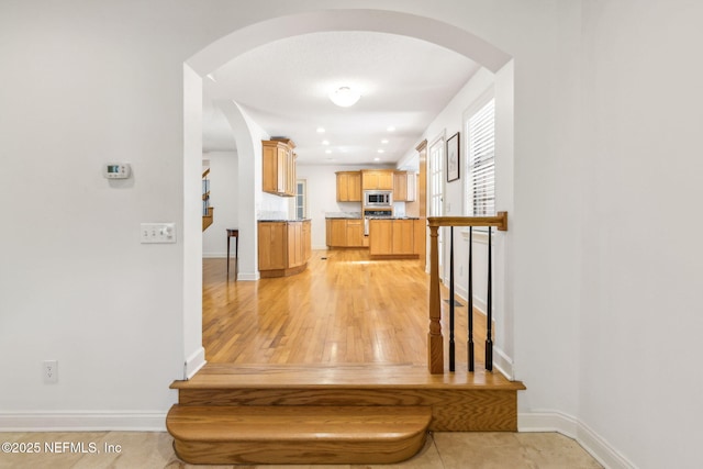 stairs with arched walkways, baseboards, and wood finished floors