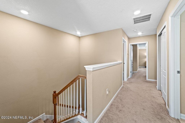 hall with a textured ceiling and light colored carpet