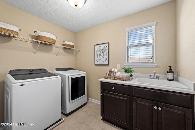 clothes washing area with washer and clothes dryer, light tile patterned floors, sink, cabinets, and a textured ceiling