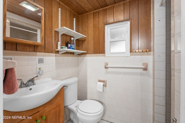 bathroom featuring toilet, wooden walls, vanity, backsplash, and tile walls