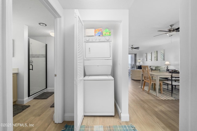 washroom featuring ceiling fan, light hardwood / wood-style floors, and stacked washer and clothes dryer