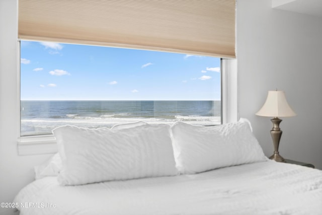 bedroom with a view of the beach, a water view, and multiple windows