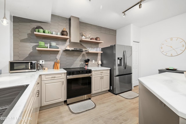 kitchen featuring rail lighting, wall chimney exhaust hood, tasteful backsplash, light hardwood / wood-style floors, and appliances with stainless steel finishes